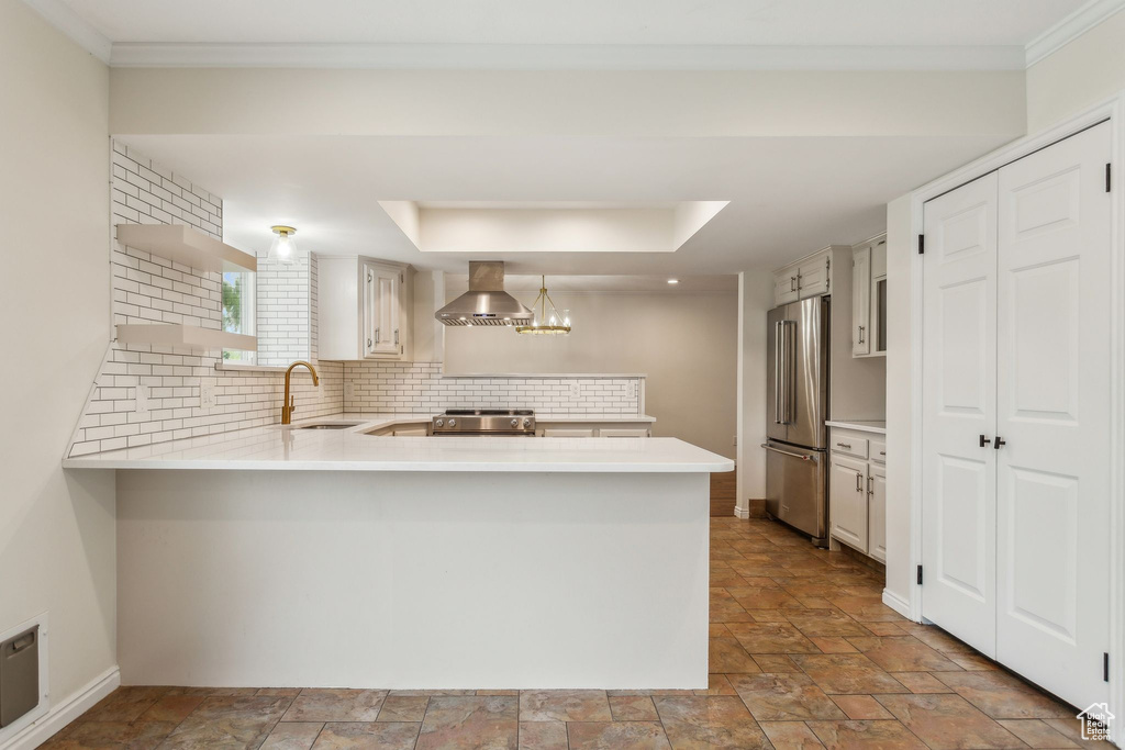 Kitchen with stainless steel appliances, a peninsula, wall chimney exhaust hood, light countertops, and a sink