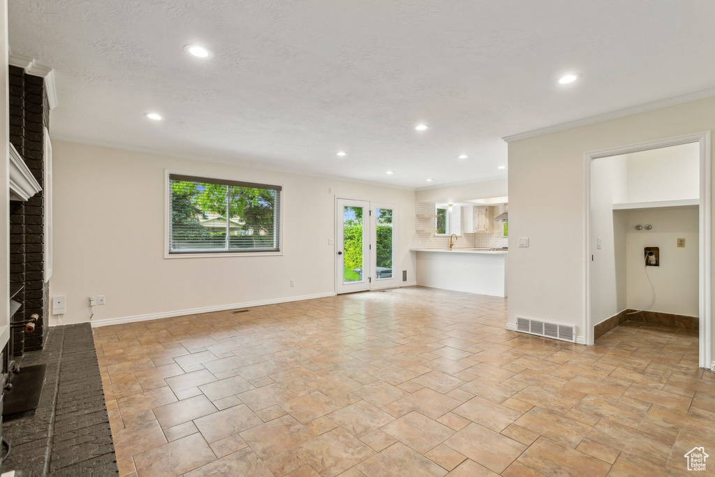 Unfurnished living room with a fireplace, recessed lighting, baseboards, stone tile floors, and ornamental molding