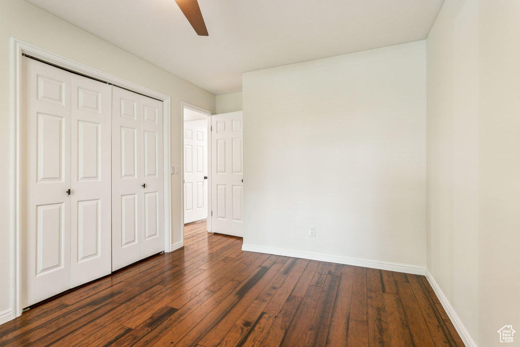 Unfurnished bedroom with baseboards, dark wood-style floors, a closet, and a ceiling fan