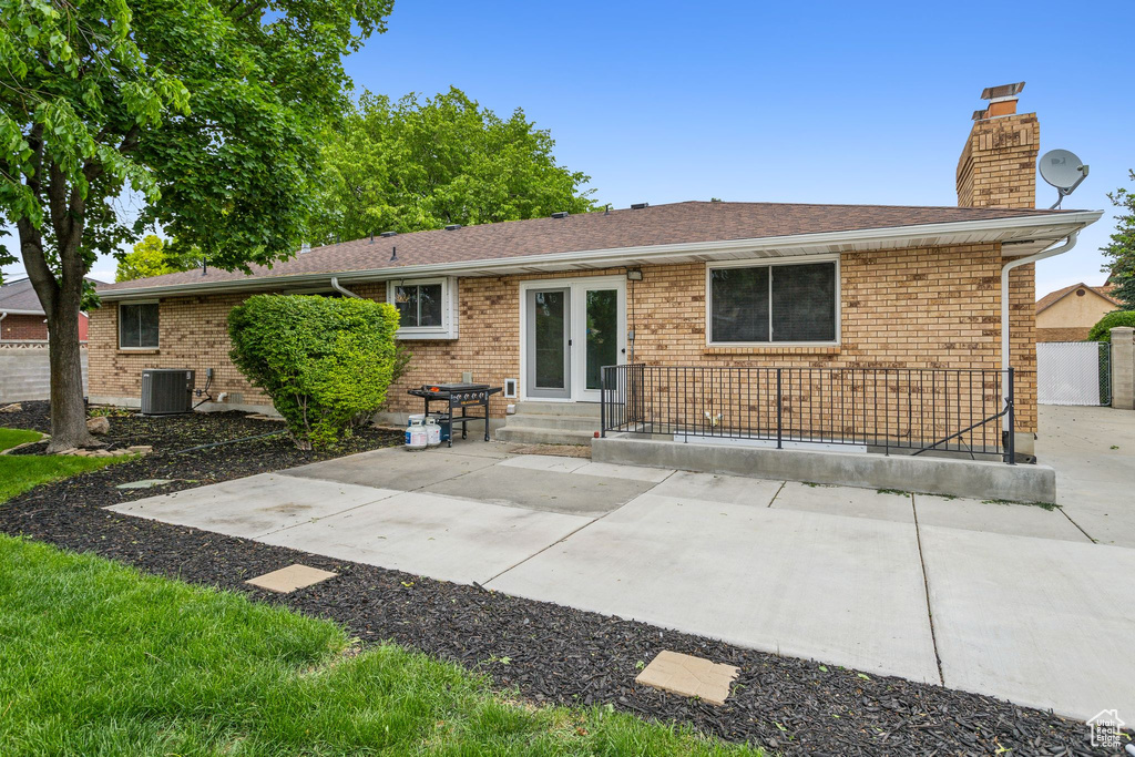 Rear view of house with central AC unit, a chimney, a patio, and brick siding