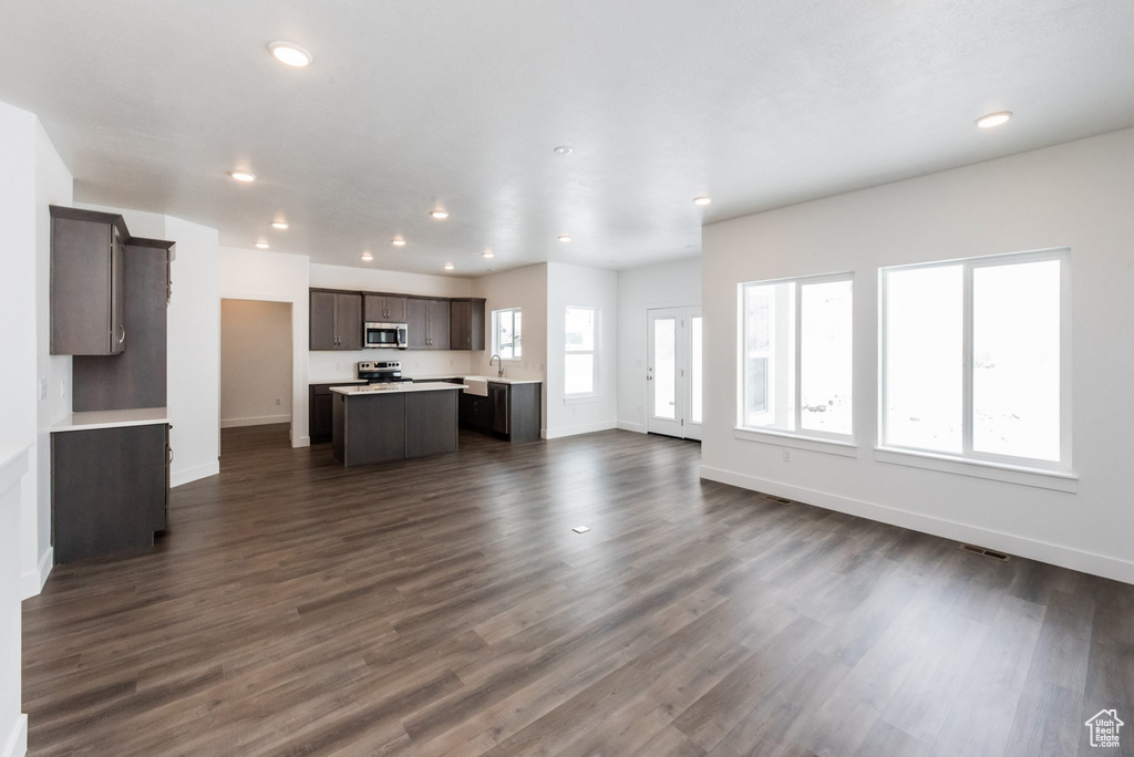Unfurnished living room featuring baseboards, a sink, recessed lighting, and dark wood-type flooring