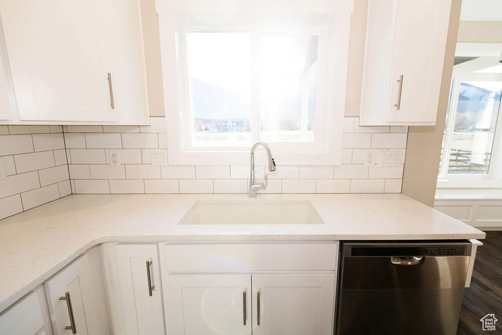 Kitchen featuring stainless steel dishwasher, a sink, white cabinets, and decorative backsplash