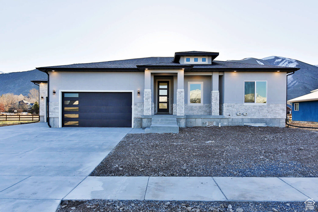 View of front of home with concrete driveway, an attached garage, stone siding, fence, and a mountain view