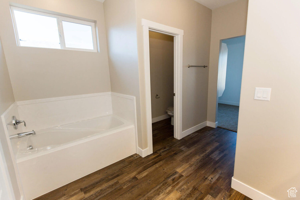 Full bath featuring toilet, a garden tub, wood finished floors, and baseboards