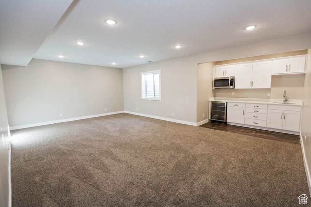 Unfurnished living room featuring wine cooler, a sink, dark carpet, baseboards, and recessed lighting