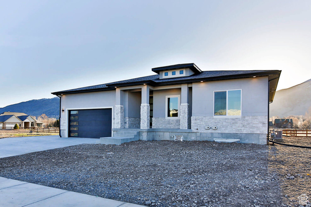 View of front of property with stone siding, fence, driveway, a garage, and a mountain view