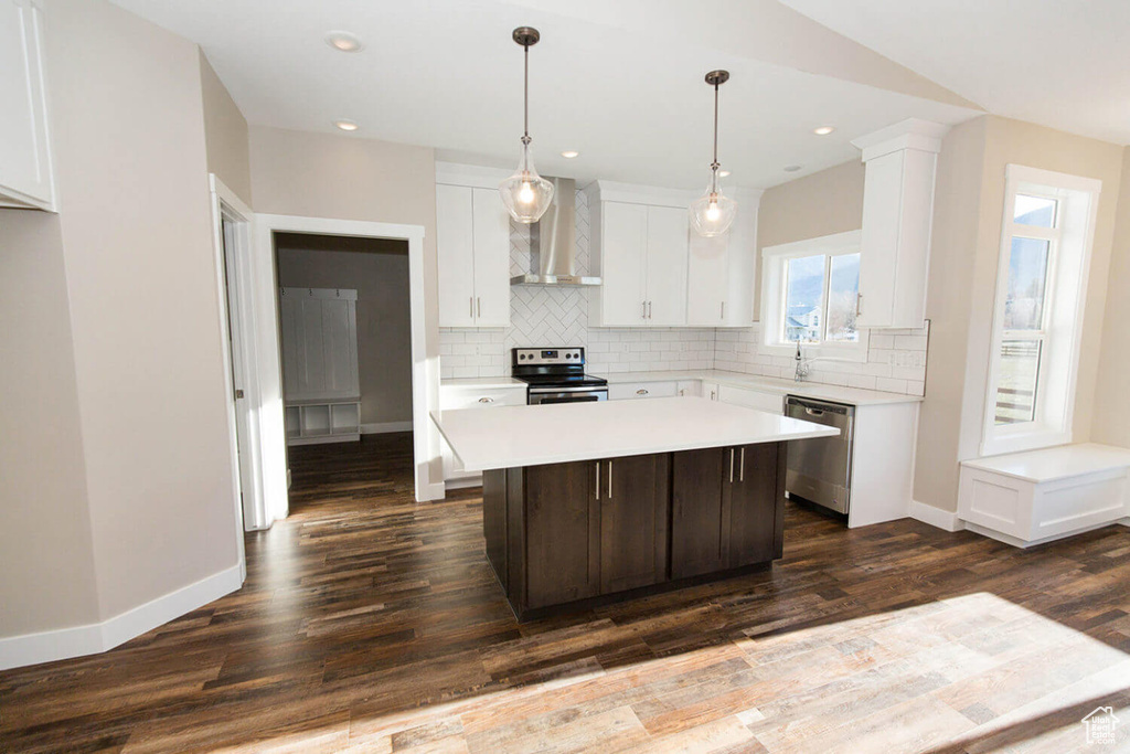 Kitchen featuring wall chimney range hood, stainless steel appliances, light countertops, tasteful backsplash, and baseboards