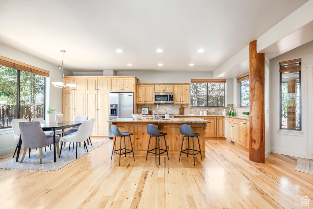 Kitchen featuring stainless steel appliances, light wood-type flooring, recessed lighting, healthy amount of natural light, and a breakfast bar