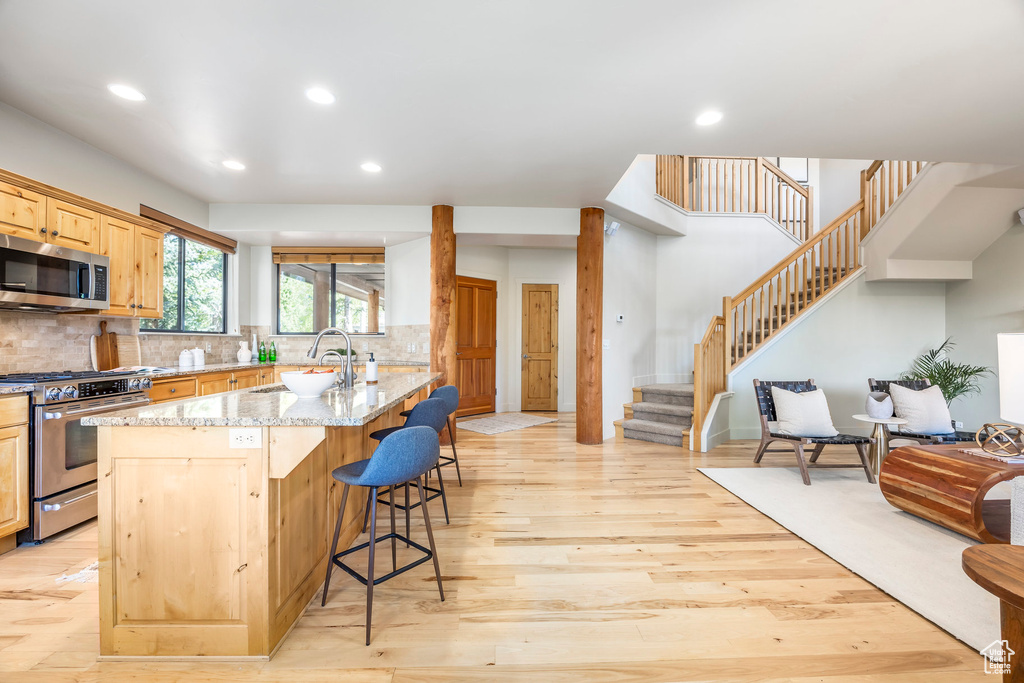 Kitchen with appliances with stainless steel finishes, a breakfast bar, light wood-style floors, recessed lighting, and light stone counters