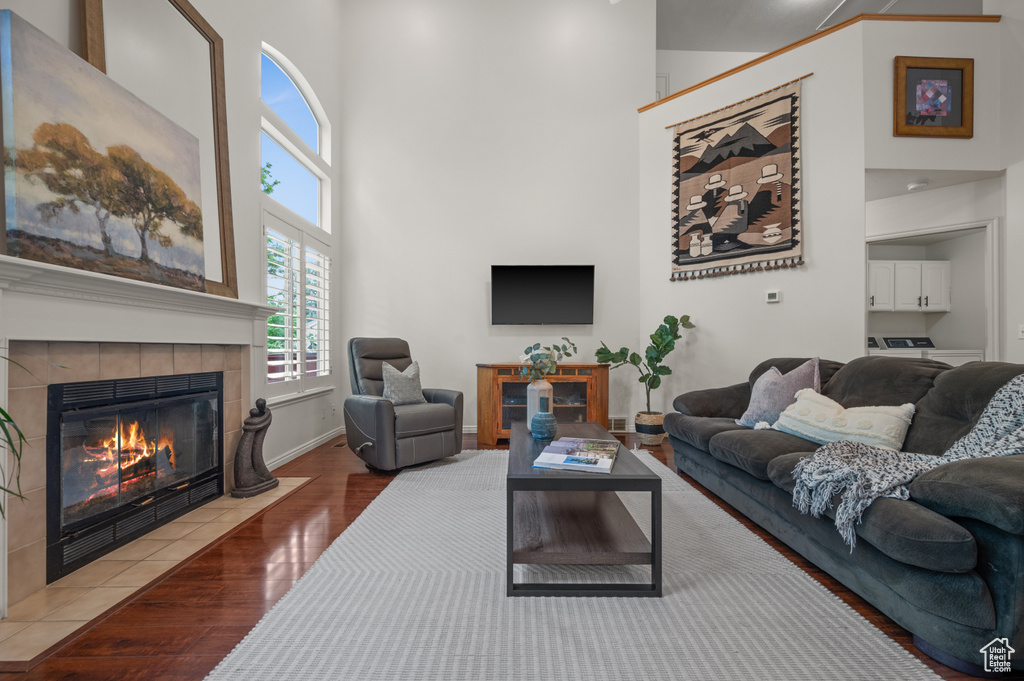 Living area featuring a towering ceiling, a tiled fireplace, wood finished floors, and baseboards