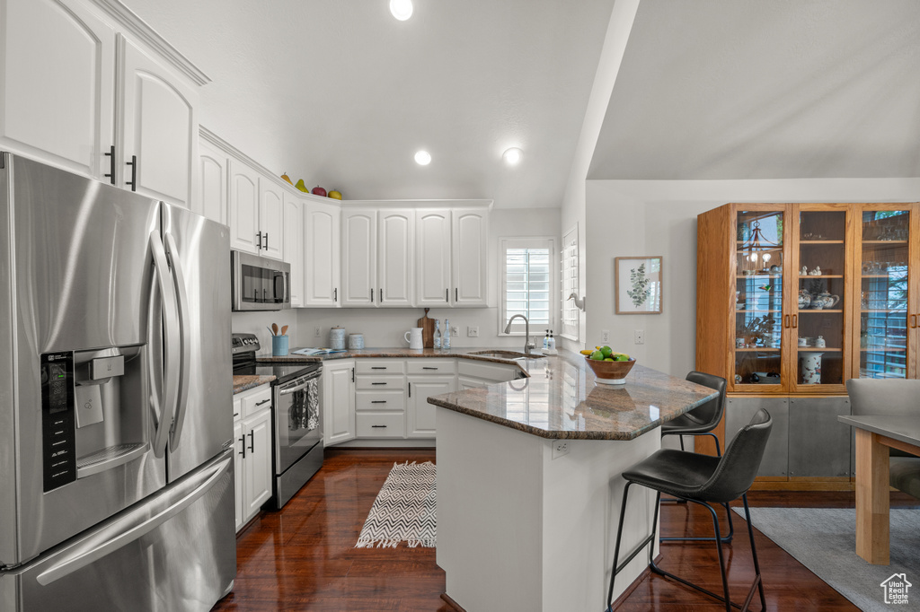 Kitchen with stainless steel appliances, a peninsula, a kitchen bar, dark stone counters, and white cabinetry