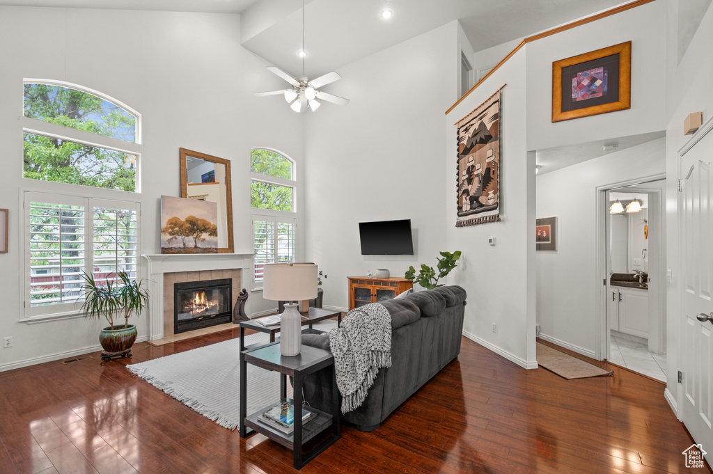 Living room featuring a towering ceiling, a fireplace, ceiling fan, wood finished floors, and baseboards