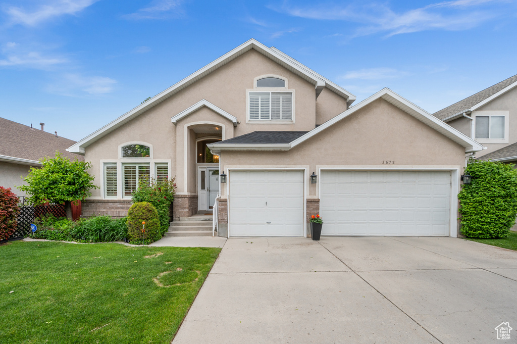 View of front facade featuring stucco siding, a front lawn, driveway, and brick siding