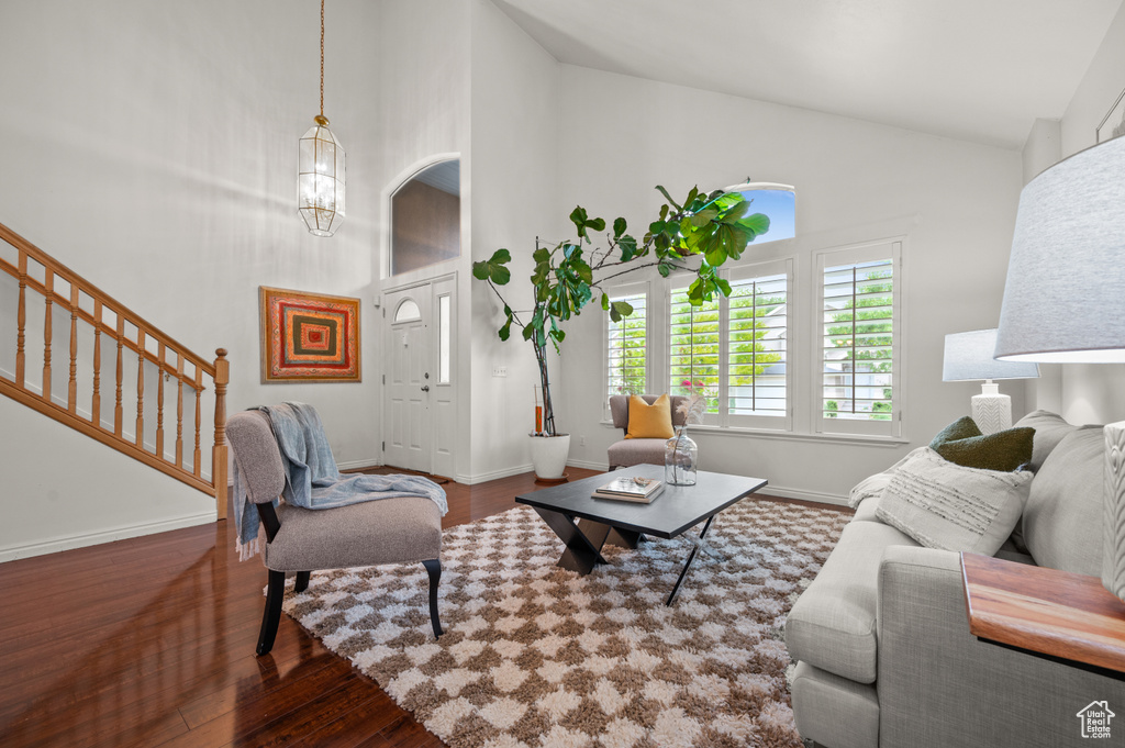 Living area with wood finished floors, high vaulted ceiling, stairs, baseboards, and a chandelier