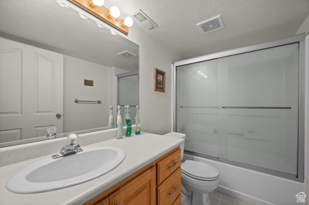 Bathroom with vanity, toilet, enclosed tub / shower combo, tile patterned floors, and a textured ceiling
