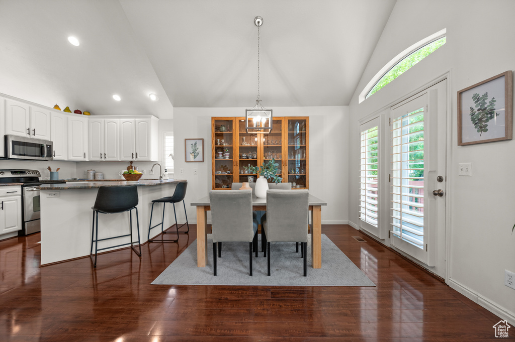 Dining space with a chandelier, recessed lighting, dark wood-style floors, high vaulted ceiling, and baseboards