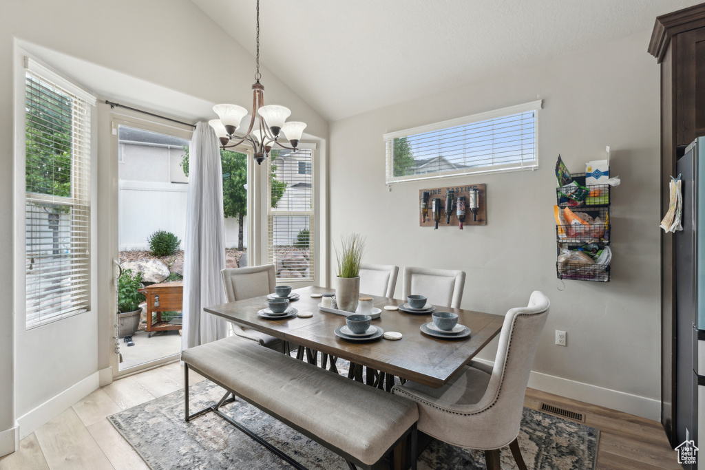 Dining room with a chandelier, light wood finished floors, lofted ceiling, and baseboards