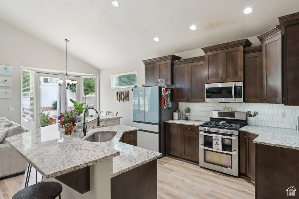 Kitchen with appliances with stainless steel finishes, a sink, tasteful backsplash, vaulted ceiling, and dark brown cabinets