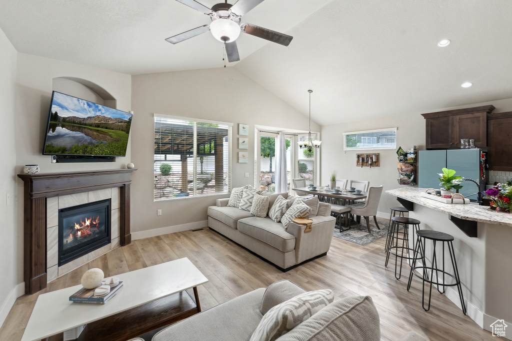 Living area with a ceiling fan, light wood-style flooring, a fireplace, lofted ceiling, and baseboards