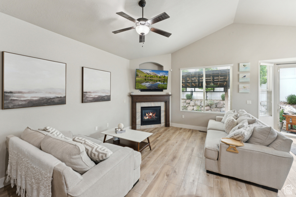 Living area with a ceiling fan, light wood-style floors, lofted ceiling, a fireplace, and baseboards