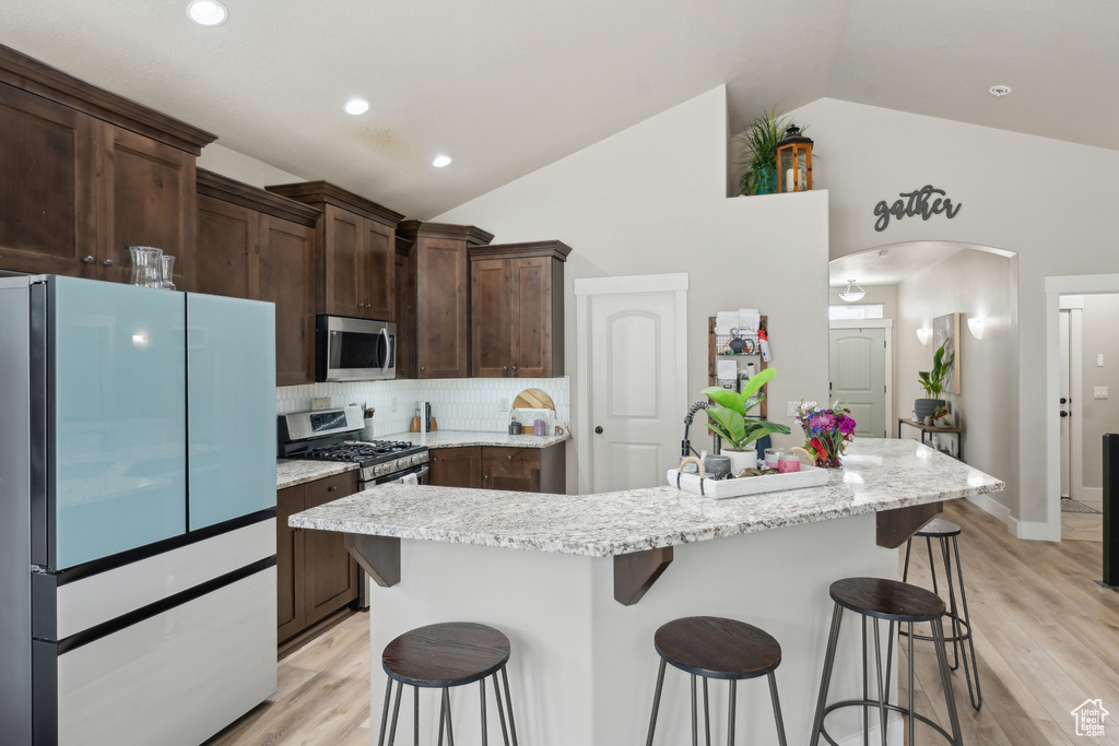 Kitchen featuring stainless steel appliances, a breakfast bar area, arched walkways, decorative backsplash, and light wood-type flooring