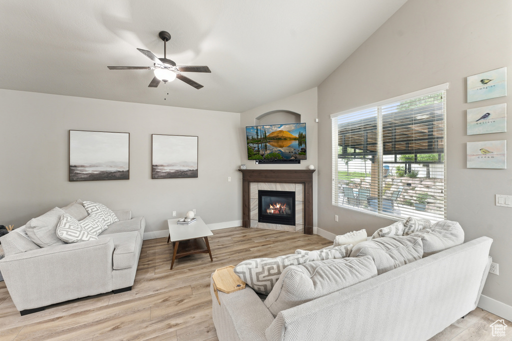 Living area featuring lofted ceiling, a ceiling fan, light wood-style floors, a fireplace, and baseboards