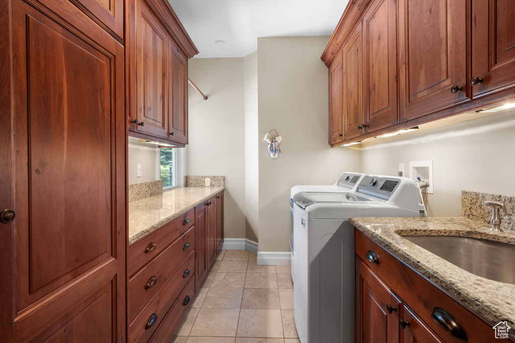 Clothes washing area featuring light tile patterned floors, a sink, cabinet space, washer and clothes dryer, and baseboards