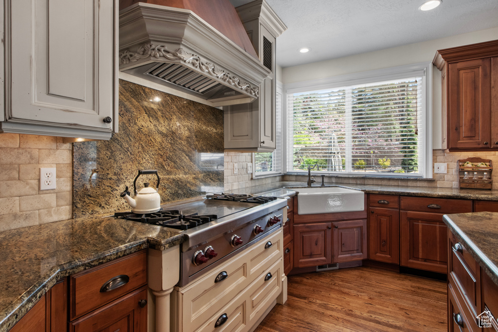 Kitchen with stainless steel gas cooktop, custom exhaust hood, a sink, dark stone countertops, and backsplash