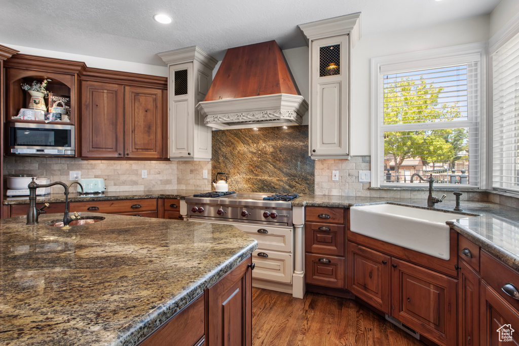 Kitchen featuring stainless steel microwave, a sink, custom range hood, and glass insert cabinets