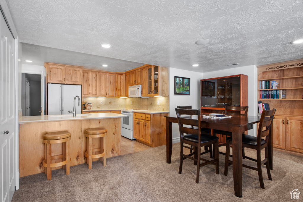 Kitchen featuring a peninsula, glass insert cabinets, a kitchen bar, white appliances, and light countertops