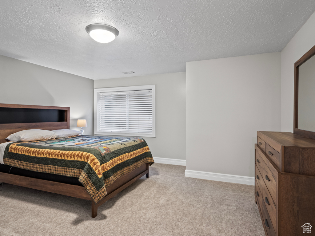 Bedroom with a textured ceiling, light carpet, baseboards, and visible vents