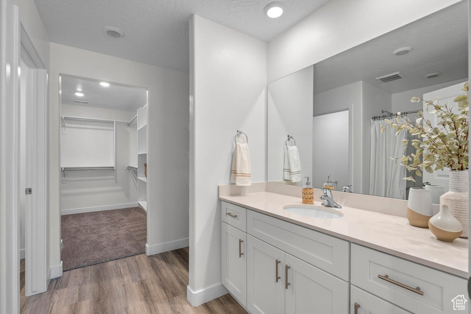 Full bath featuring vanity, wood finished floors, baseboards, a shower with shower curtain, and a spacious closet
