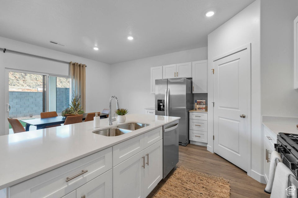Kitchen with a sink, stainless steel appliances, white cabinetry, light countertops, and recessed lighting