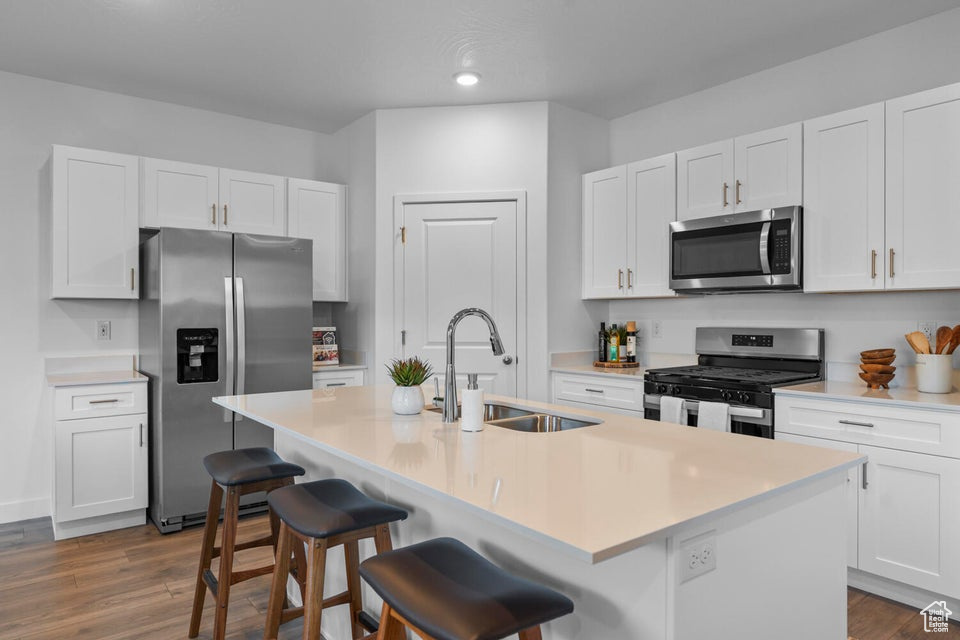 Kitchen with appliances with stainless steel finishes, a sink, dark wood-type flooring, a kitchen bar, and recessed lighting