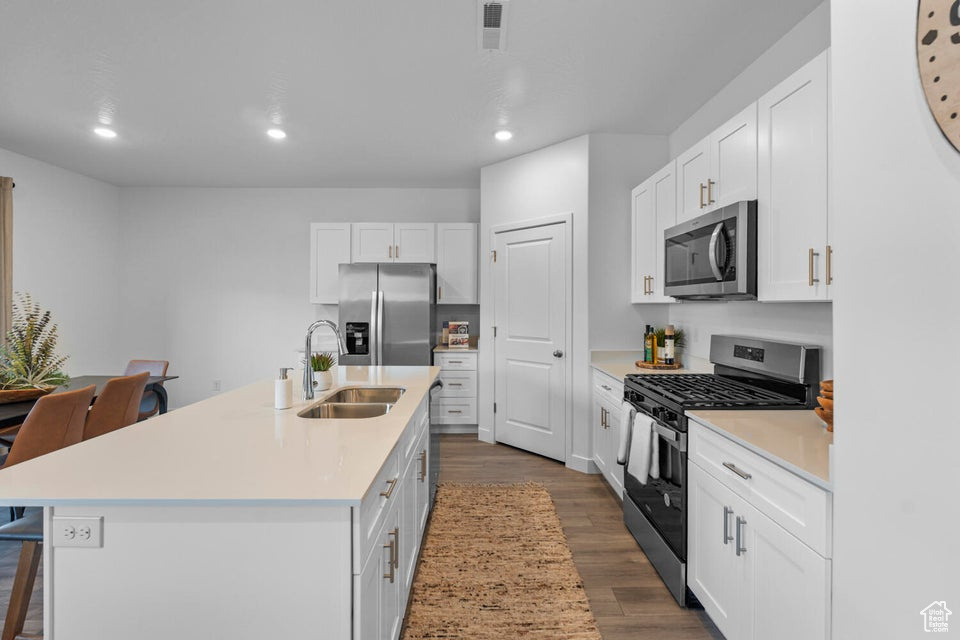 Kitchen with appliances with stainless steel finishes, a sink, recessed lighting, dark wood finished floors, and white cabinets