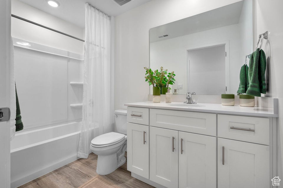 Bathroom with toilet, wood finished floors, vanity, and shower / tub combo with curtain