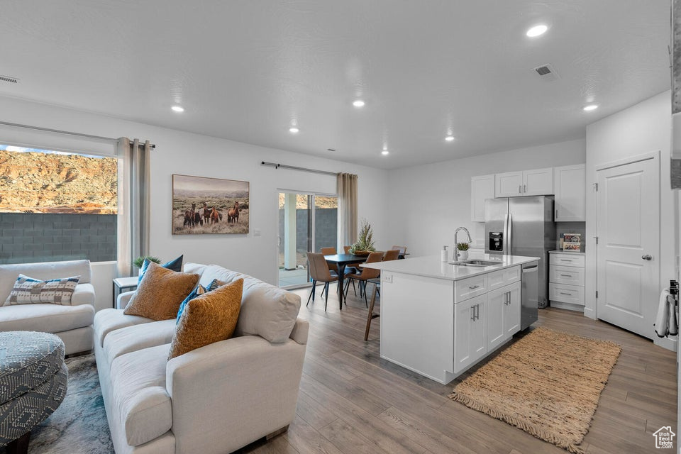 Kitchen featuring open floor plan, a sink, stainless steel dishwasher, white cabinetry, and recessed lighting