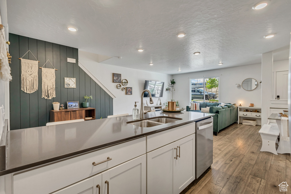 Kitchen featuring stainless steel dishwasher, a sink, white cabinets, dark countertops, and wood finished floors