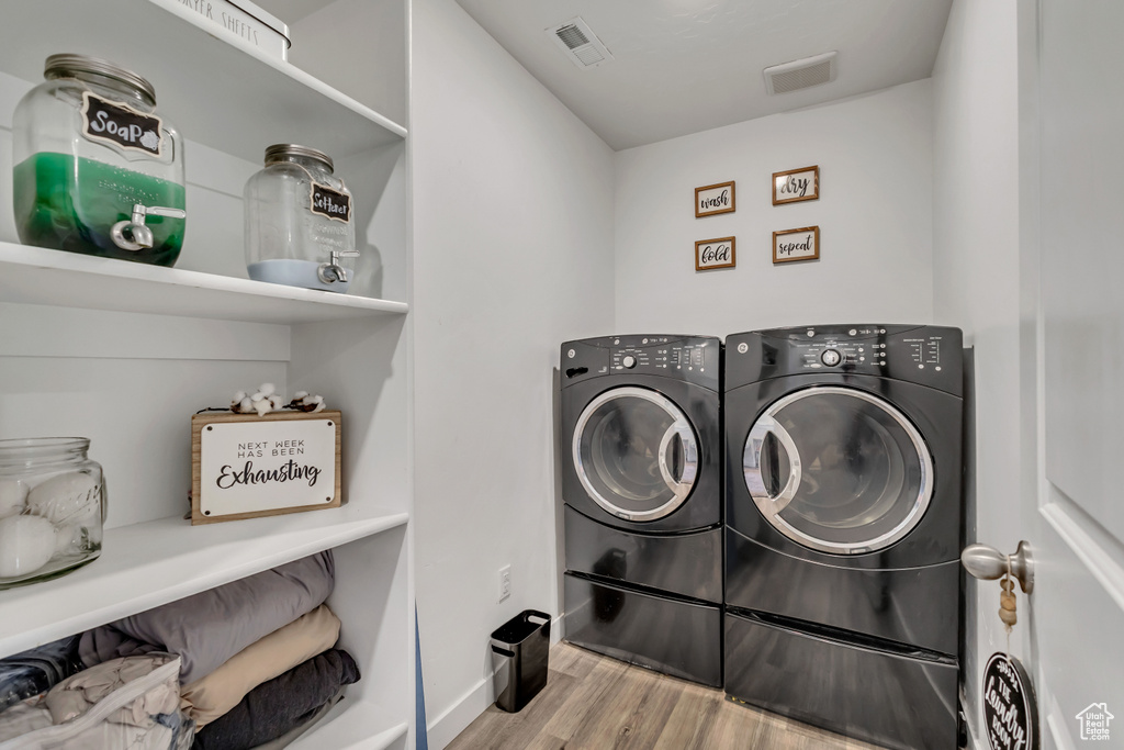 Clothes washing area featuring washing machine and clothes dryer, wood finished floors, and baseboards
