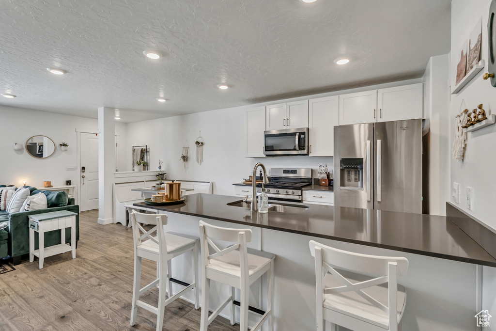 Kitchen featuring stainless steel appliances, a sink, dark countertops, light wood finished floors, and a kitchen breakfast bar