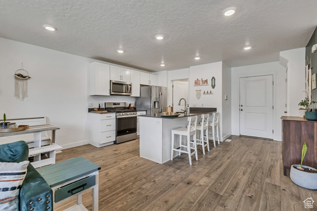 Kitchen with appliances with stainless steel finishes, dark countertops, a breakfast bar area, light wood-type flooring, and white cabinets