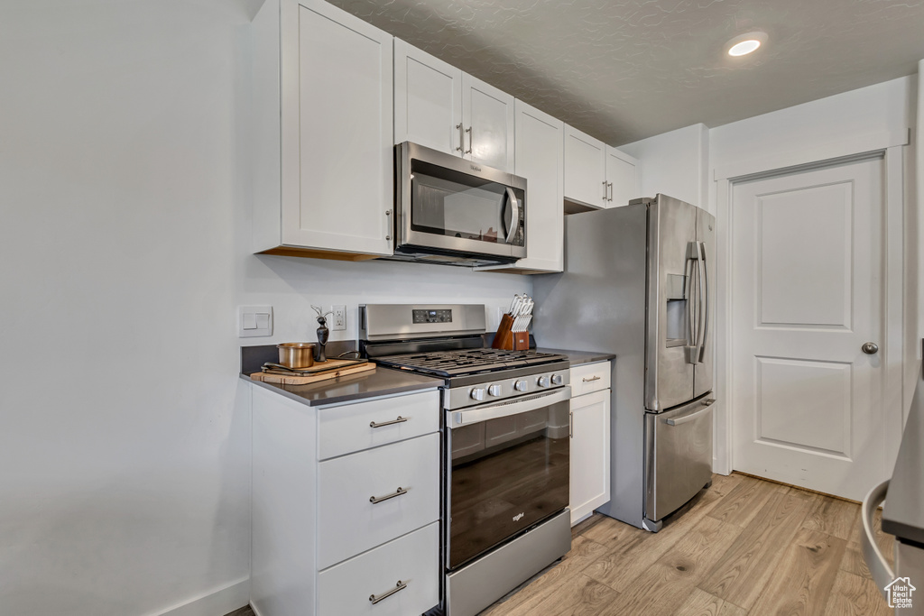 Kitchen with stainless steel appliances, light wood-style flooring, dark countertops, white cabinets, and recessed lighting