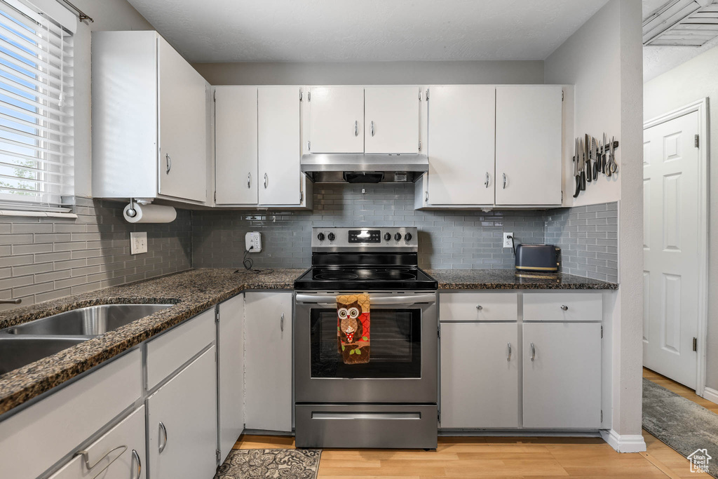 Kitchen with stainless steel electric range, under cabinet range hood, white cabinets, tasteful backsplash, and dark stone counters