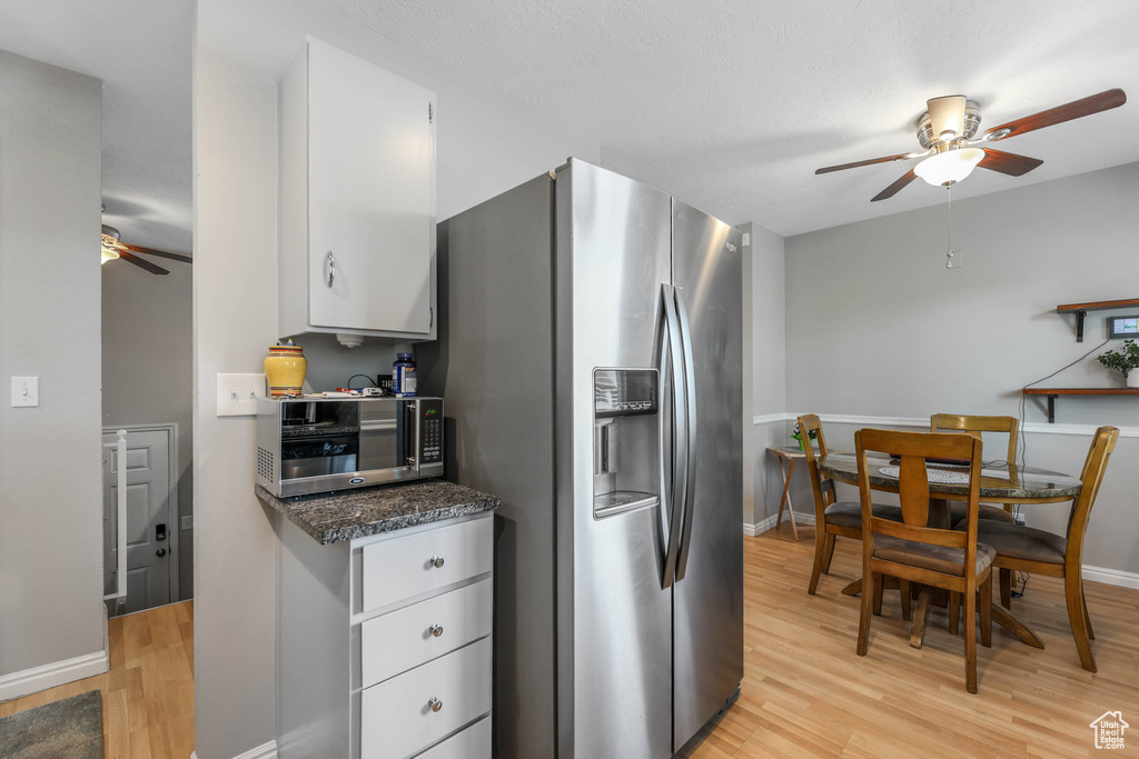 Kitchen with a ceiling fan, appliances with stainless steel finishes, light wood-style floors, white cabinetry, and baseboards