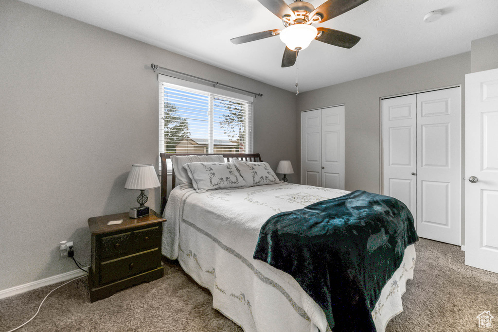 Bedroom featuring light colored carpet, multiple closets, baseboards, and ceiling fan