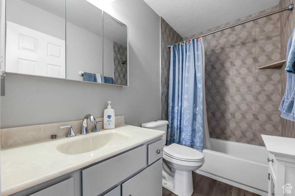 Full bathroom with wood finished floors, vanity, toilet, shower / tub combo with curtain, and a textured ceiling
