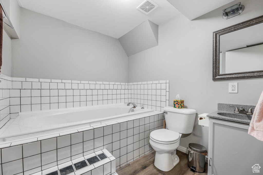 Bathroom featuring wood finished floors, toilet, a garden tub, vanity, and baseboards