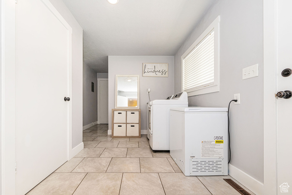 Clothes washing area with washing machine and clothes dryer, light tile patterned flooring, and baseboards