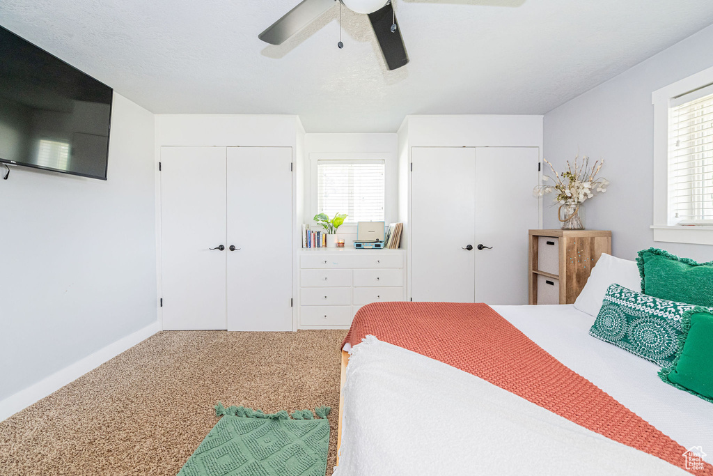 Carpeted bedroom with two closets, a ceiling fan, and baseboards