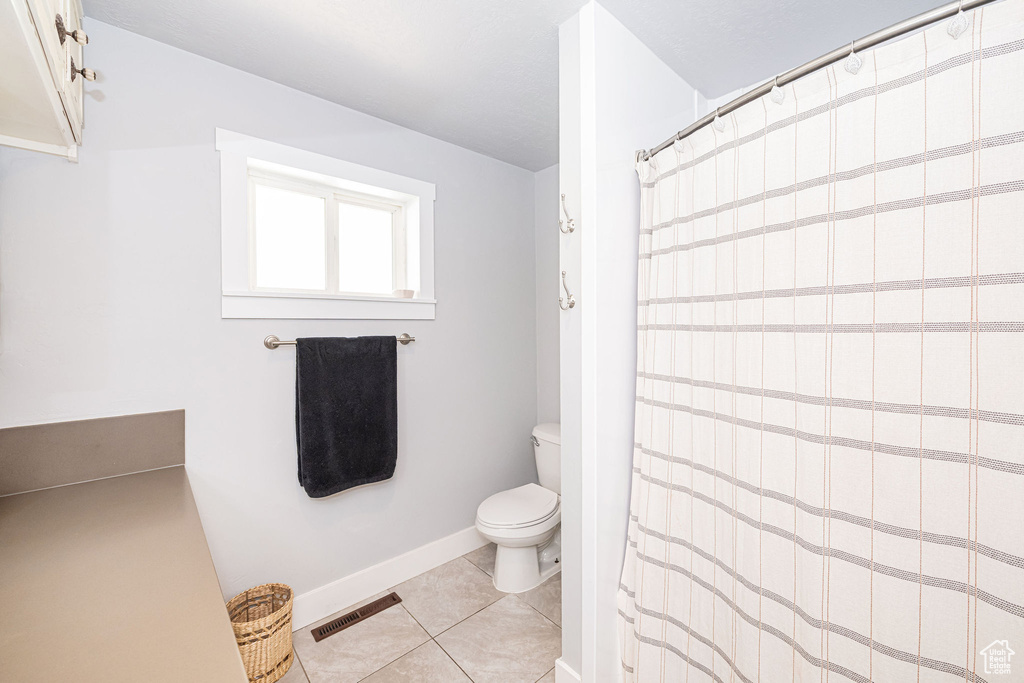 Bathroom featuring toilet, tile patterned floors, a shower with shower curtain, and baseboards